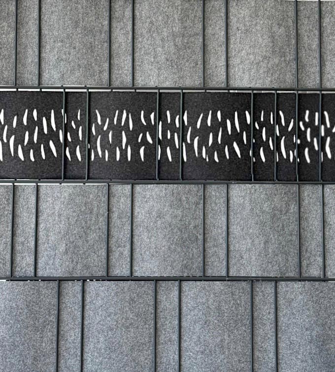Detailansicht eines modularen, grauen Akustik-Wandpaneels aus Filz mit horizontalem schwarzem Streifen und dekorativen, tropfenförmigen Ausstanzungen zur Schallabsorption.