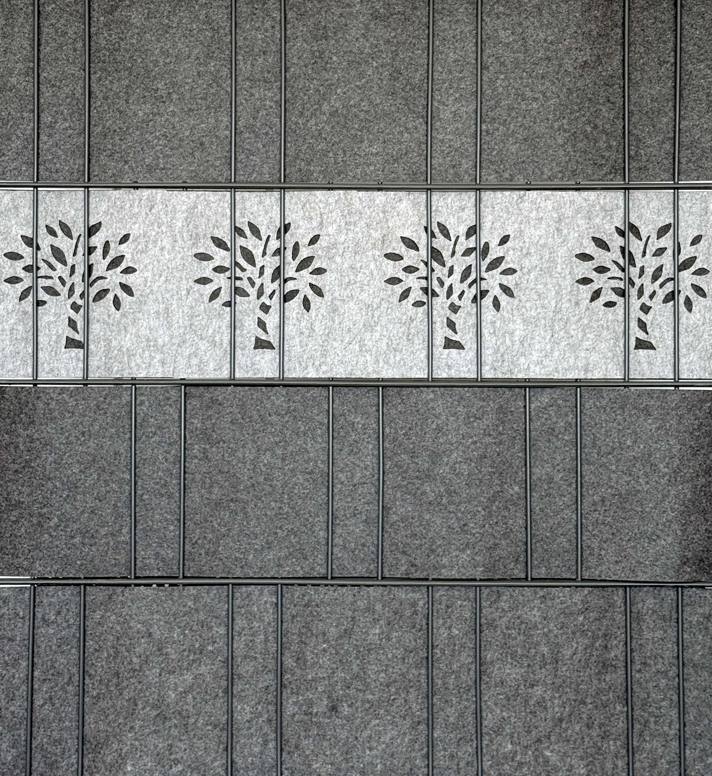 Graue Filz-Akustikpaneele für die Wand, mittlere Reihe mit ausgestanztem Baum-Motiv als dekoratives Designelement.