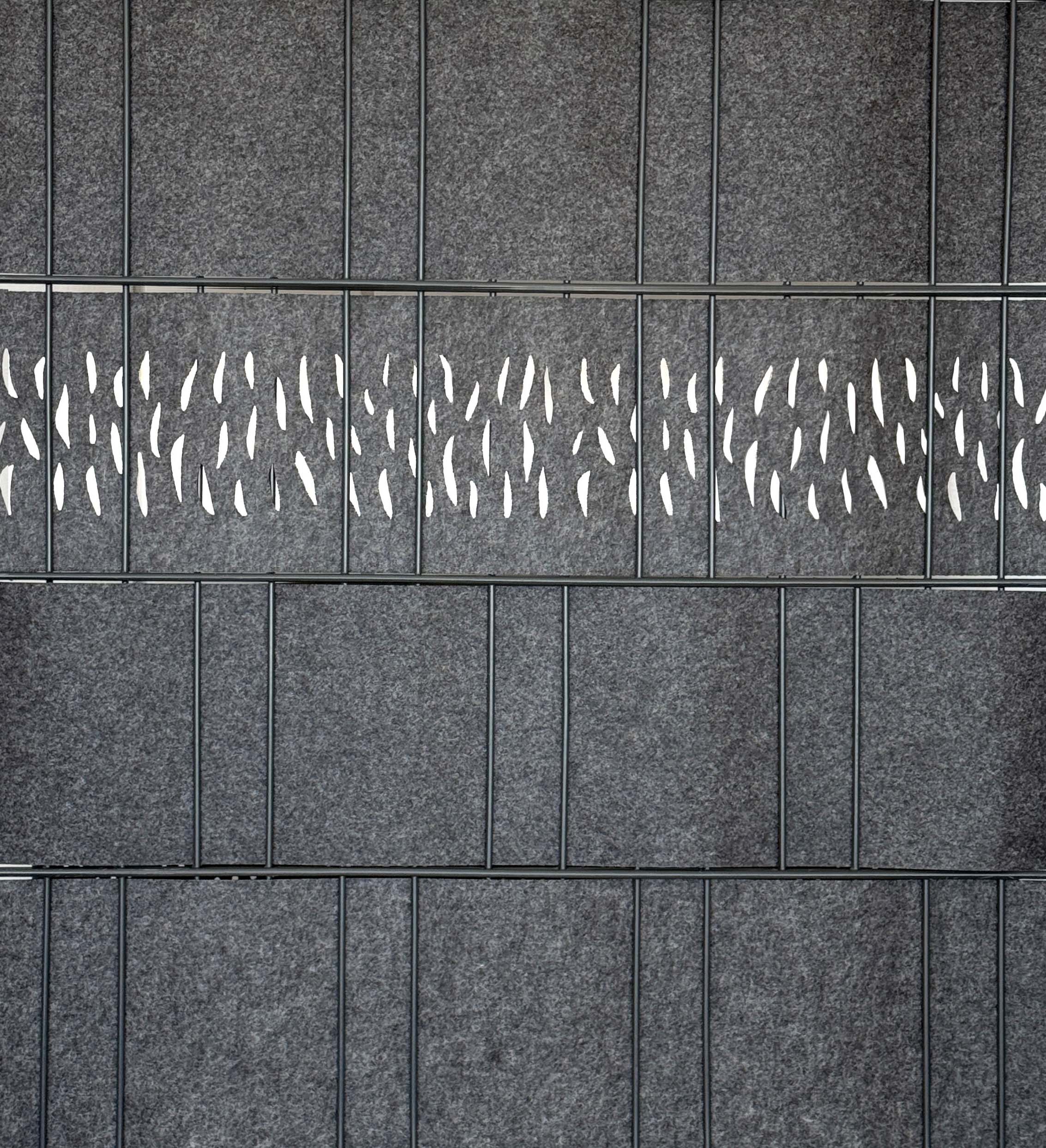 Detailansicht einer grauen Akustik-Trennwand aus Filz mit filigranen Ausschnitten, montiert in einem Metallrahmen als Raumteiler